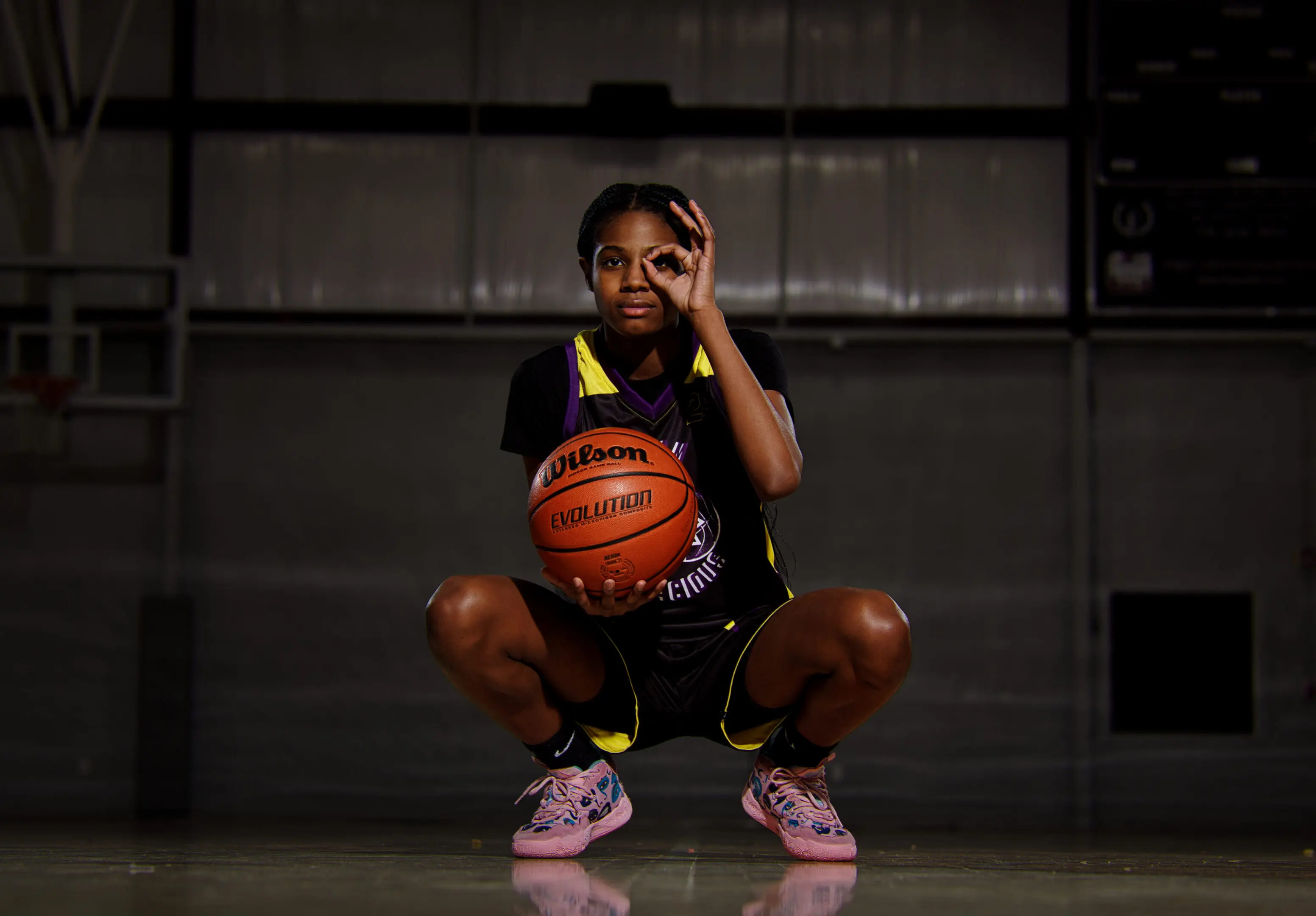 A girl squatting with her basketball in front of the camera.